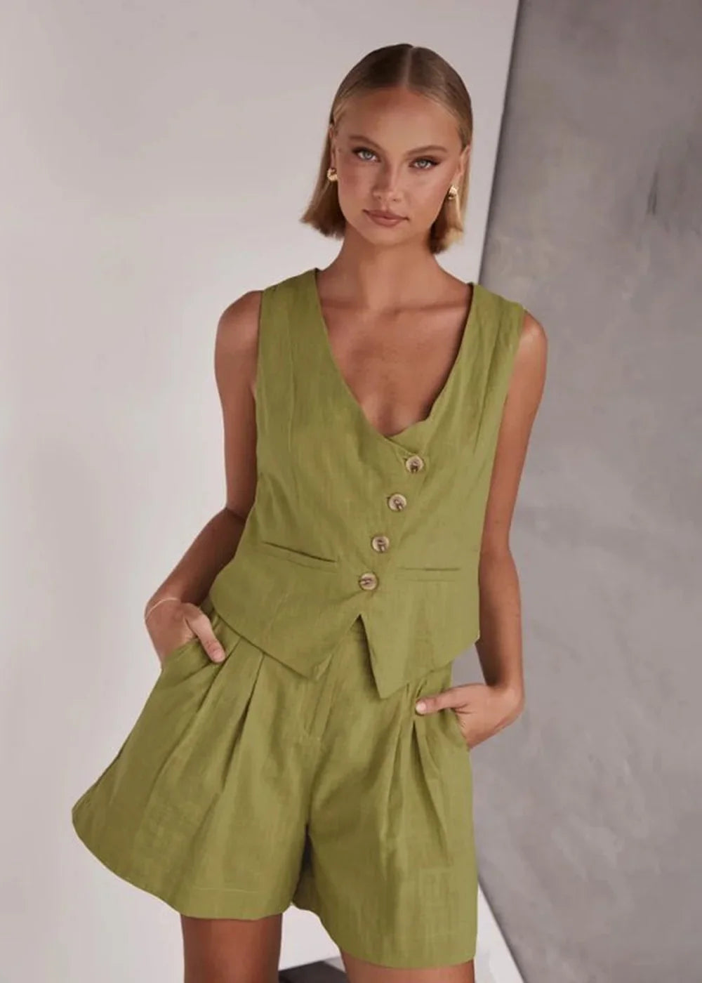 Model in lime green linen-blend vest and pleated shorts, showing texture and button details.