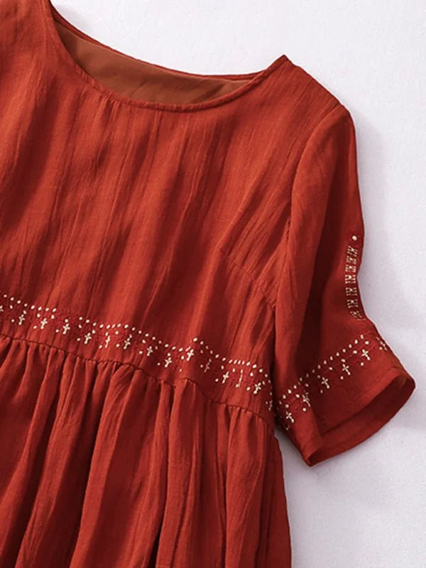 Rust orange linen-blend dress with embroidered trim and tiered skirt.