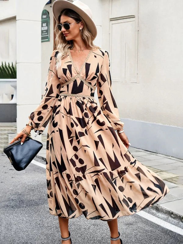 Beige midi dress with abstract black print, V-neck, and tiered skirt, worn by a model with a hat.