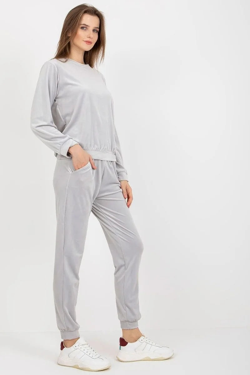 Light gray velour tracksuit on a model, featuring a long-sleeved top and matching pants with pockets.