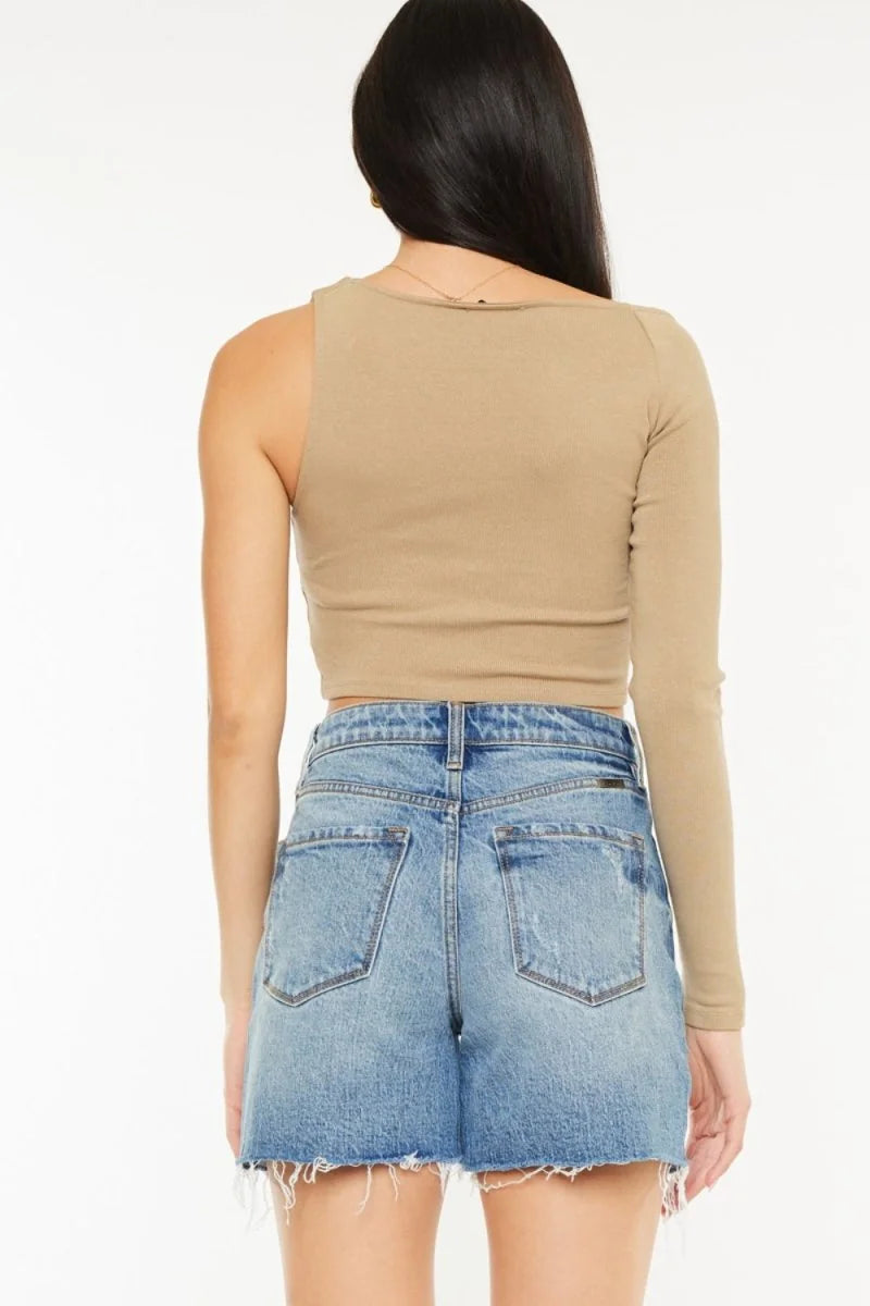 Back view of light wash distressed denim shorts with frayed hem and tan one-sleeve crop top.