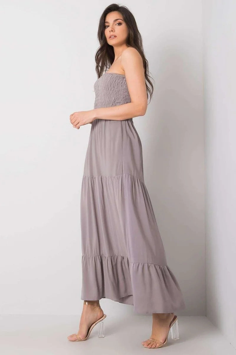 A woman in a grey strapless tiered maxi dress with a smocked bodice and clear heeled sandals.