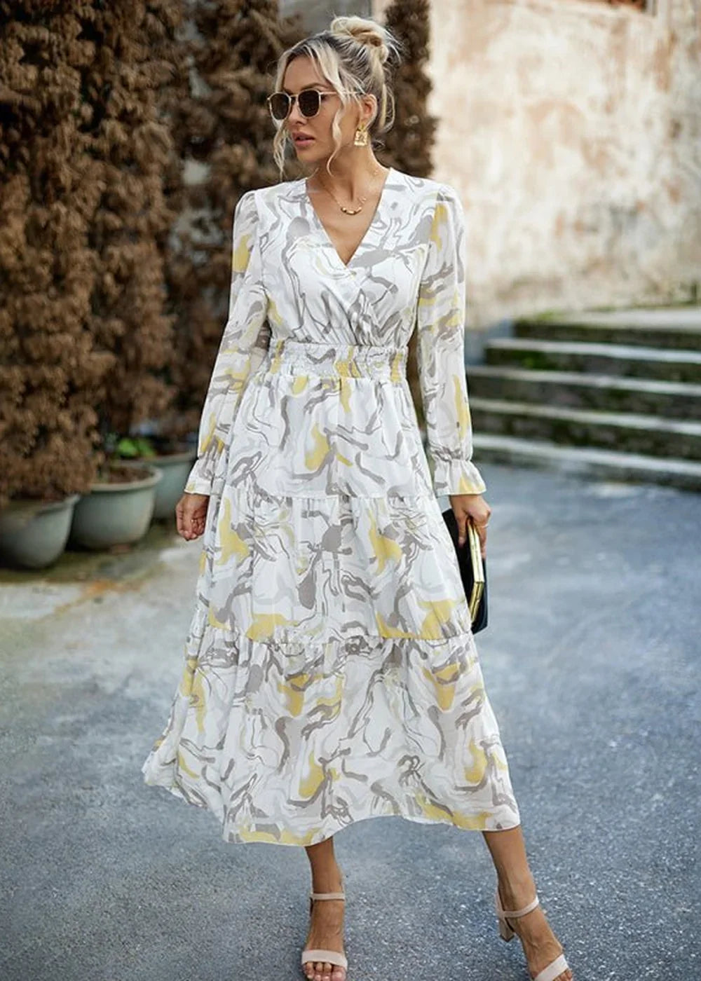 Woman in a flowy white dress with a gray and yellow abstract print, v-neck, and tiered skirt.