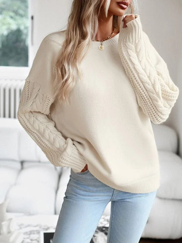 Cream cable-knit sweater with intricate sleeve detailing, worn by a model with light wash jeans.