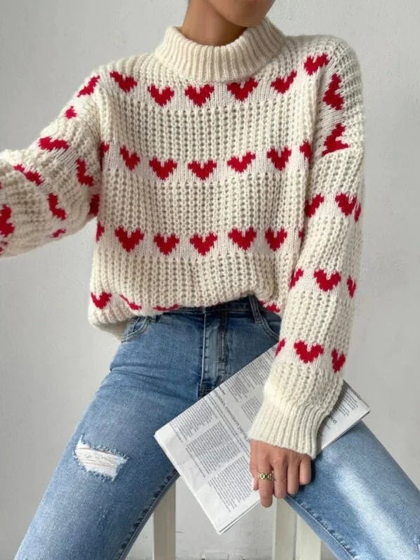Cream knit sweater with red hearts pattern, long sleeves, and crew neck, worn with distressed denim jeans.