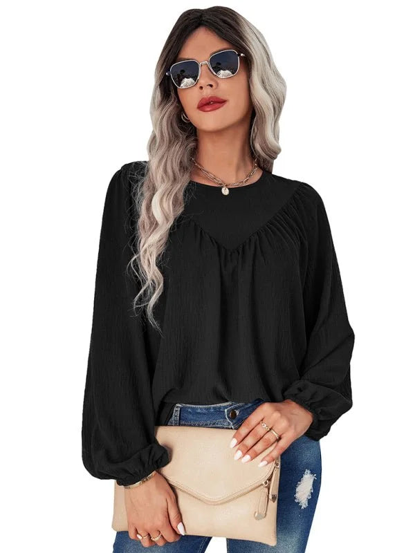 Black peasant blouse with textured fabric and puff sleeves, worn by a model with sunglasses and a clutch.