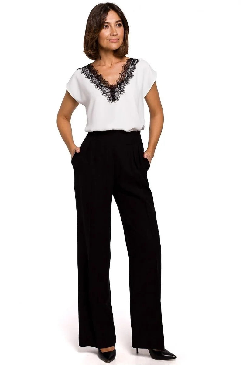 Woman in white V-neck lace-trim top and black wide-leg pants.