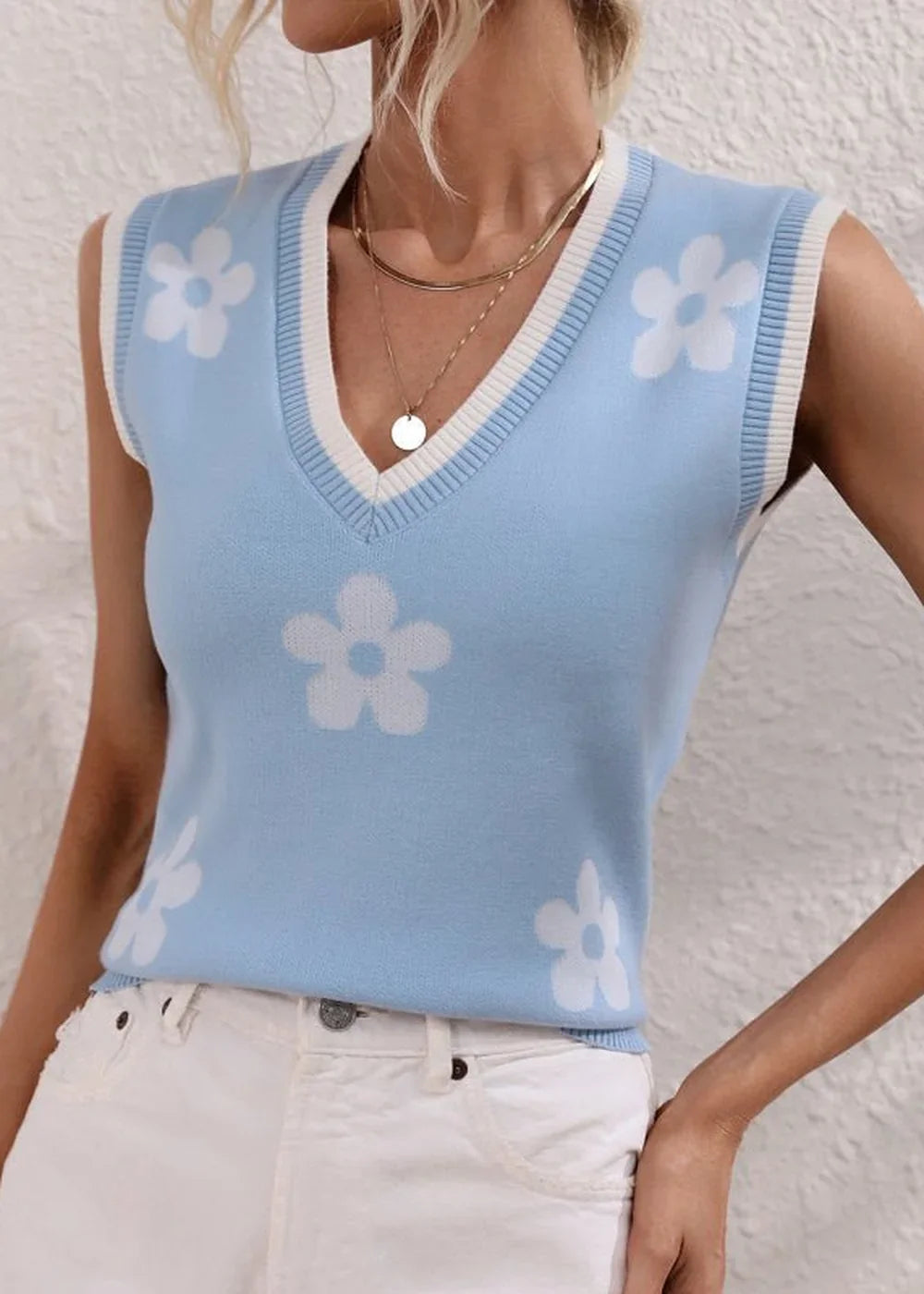 Light blue knit vest with white floral pattern and white trim, on a model.
