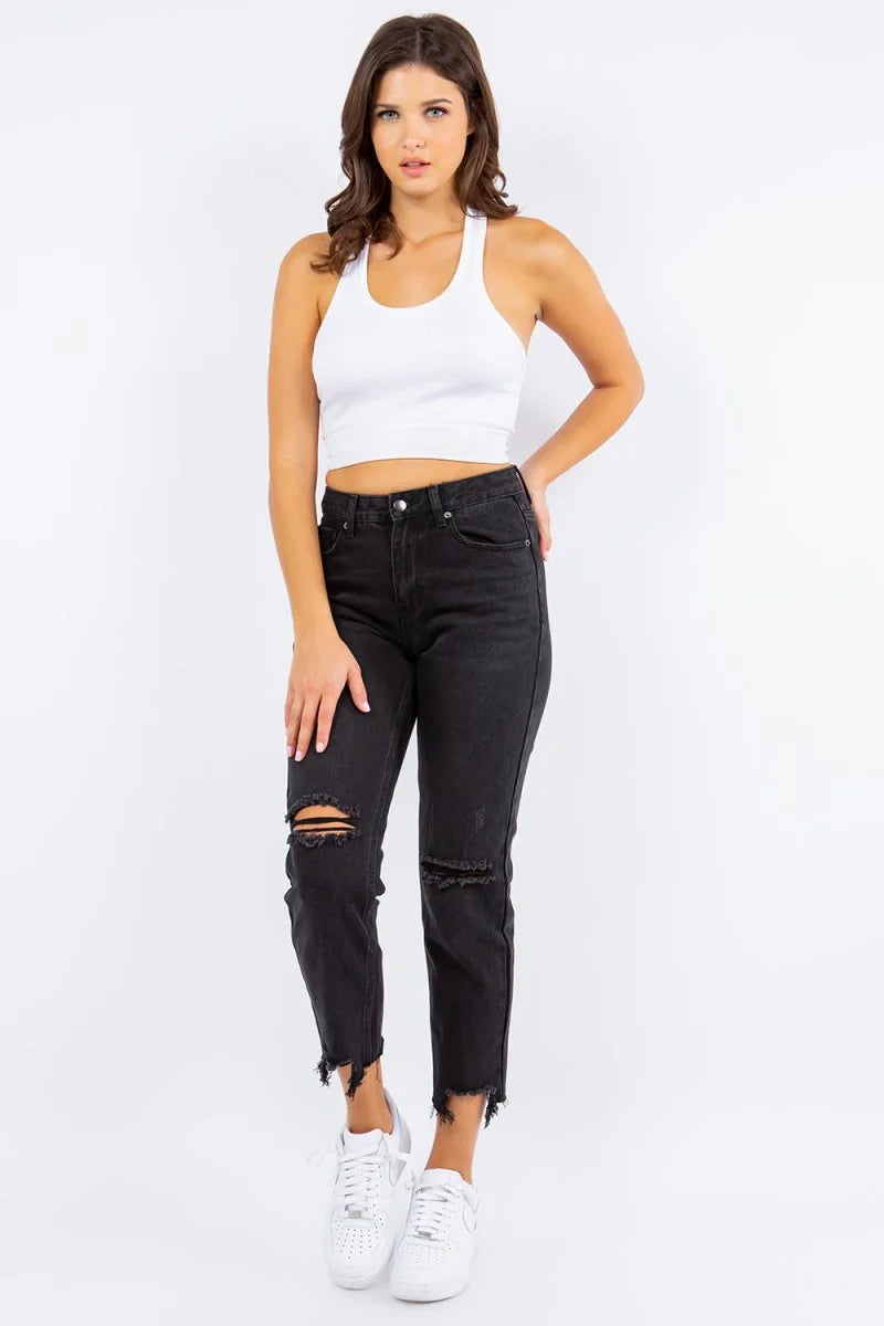 Black high-waisted distressed denim jeans with frayed hem on model.