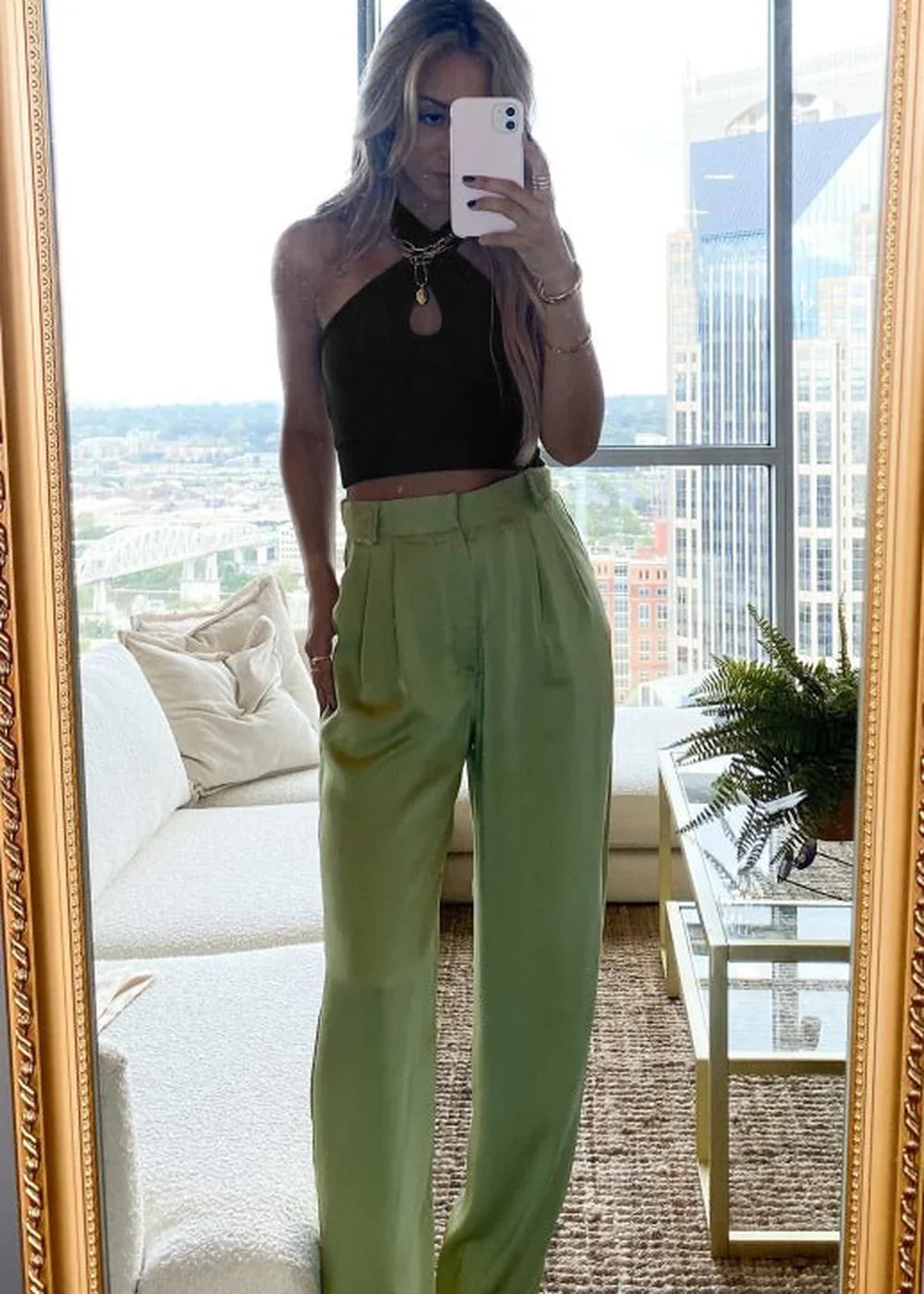 Woman in black halter crop top and lime green satin wide-leg pants, holding phone.