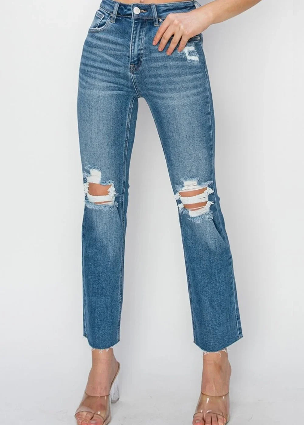 Medium wash distressed denim jeans with a frayed hem and ripped knees, worn on a model.
