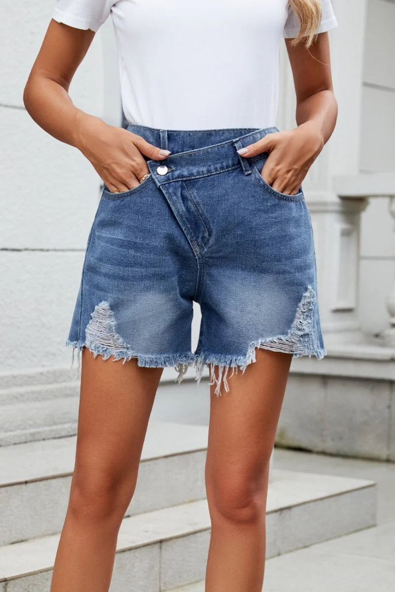 Distressed denim shorts with a frayed hem and asymmetrical front closure.