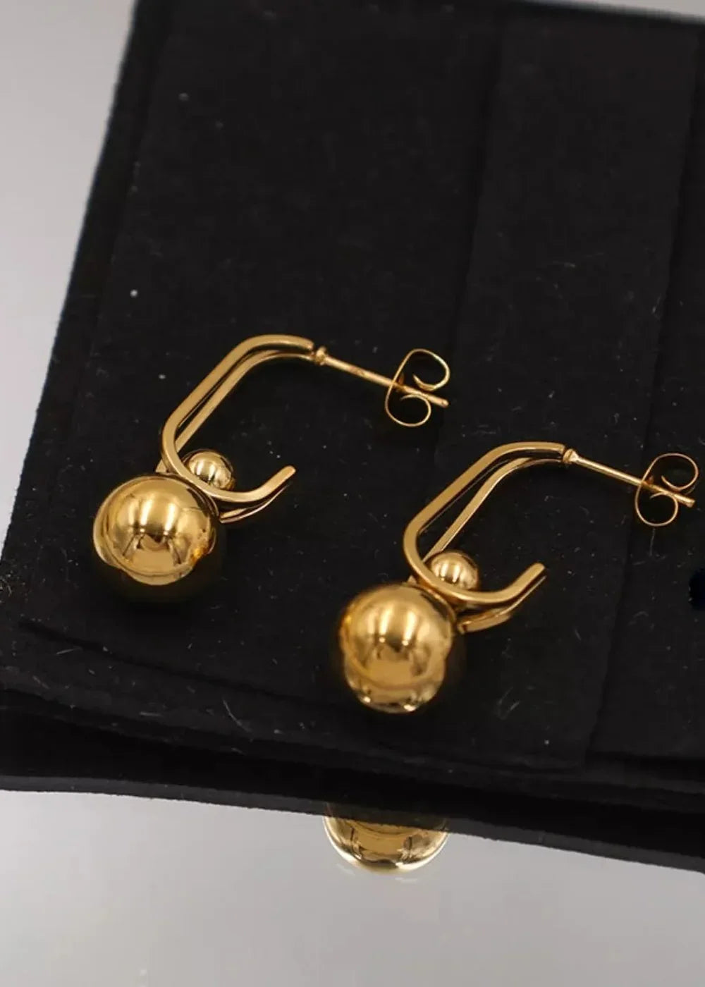 Close-up of polished 18K gold-plated hoop earrings with dangling ball charms.
