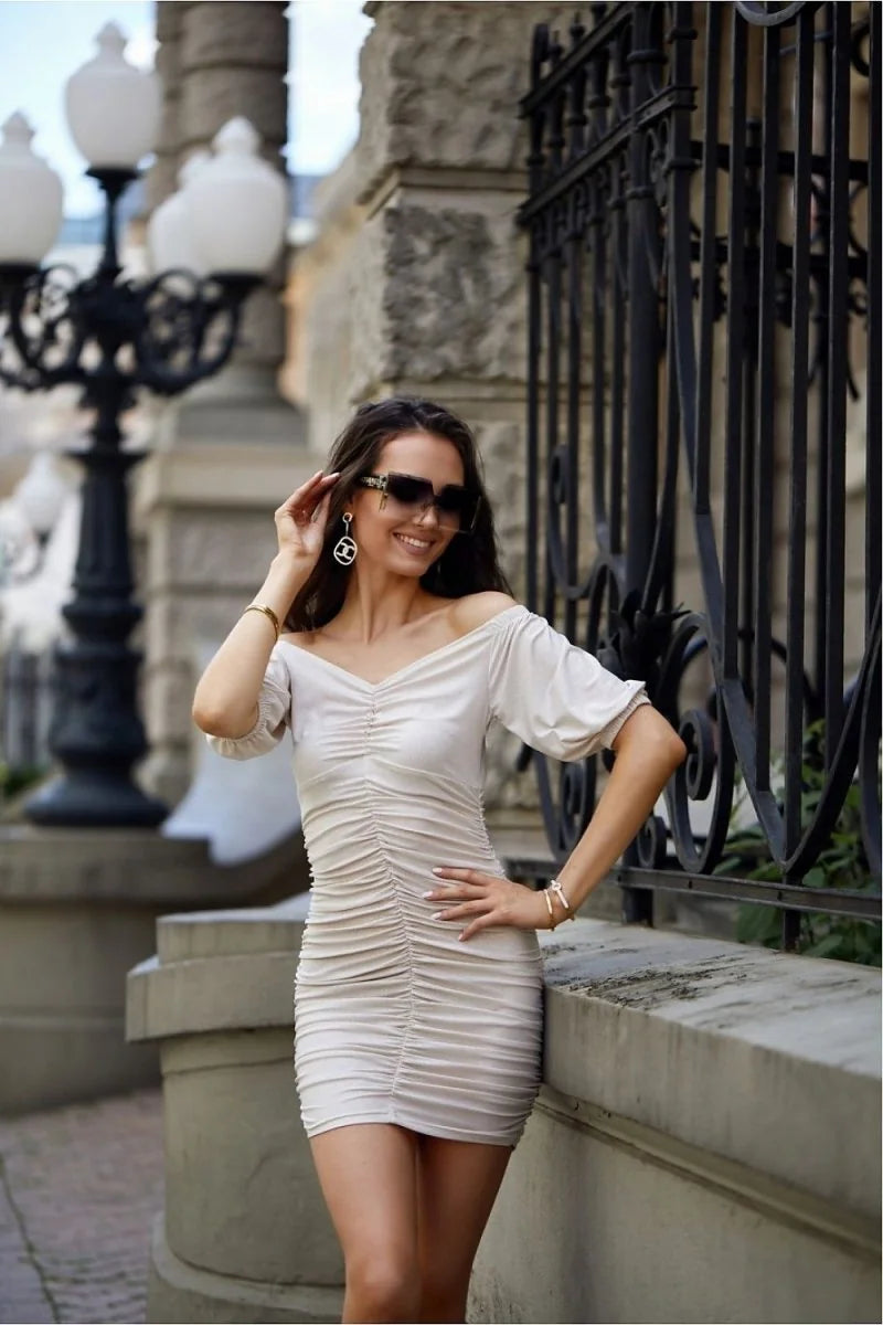 Off-the-shoulder ruched dress in a light beige, fitted style with a sweetheart neckline.
