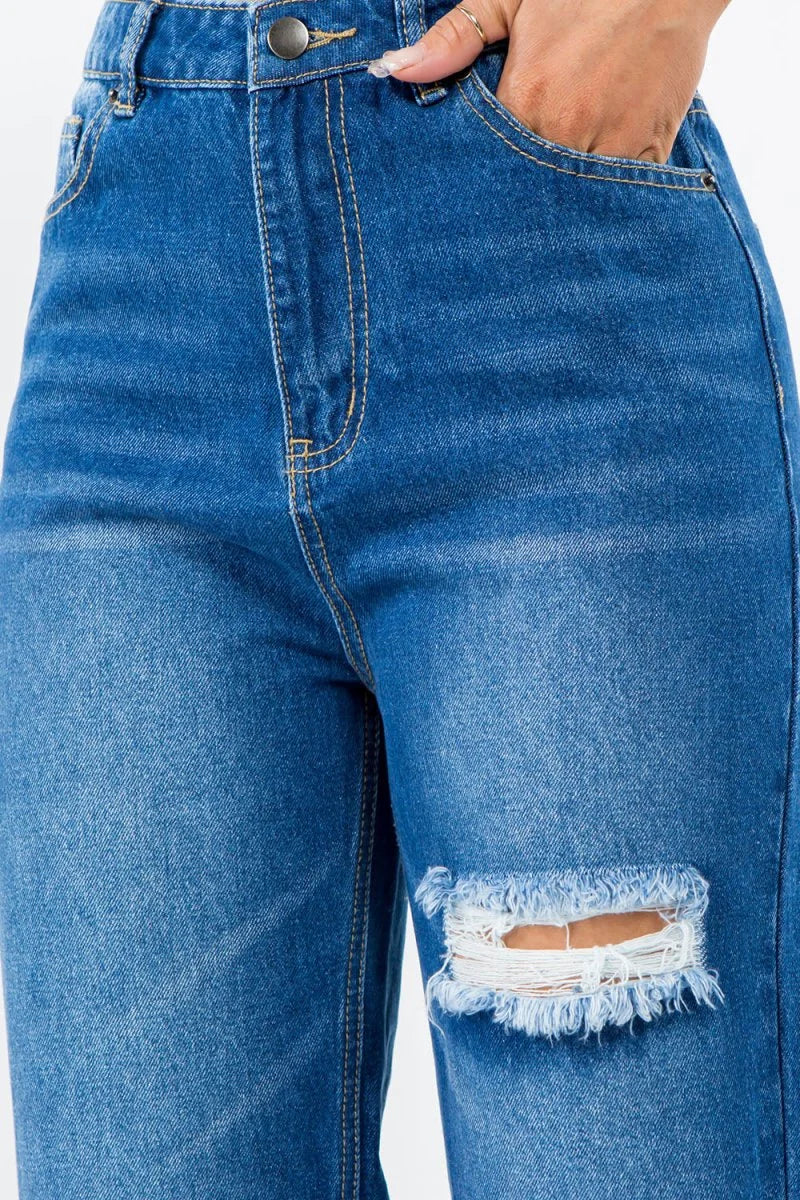 Close-up of distressed blue denim jeans with a ripped knee detail and frayed edges.