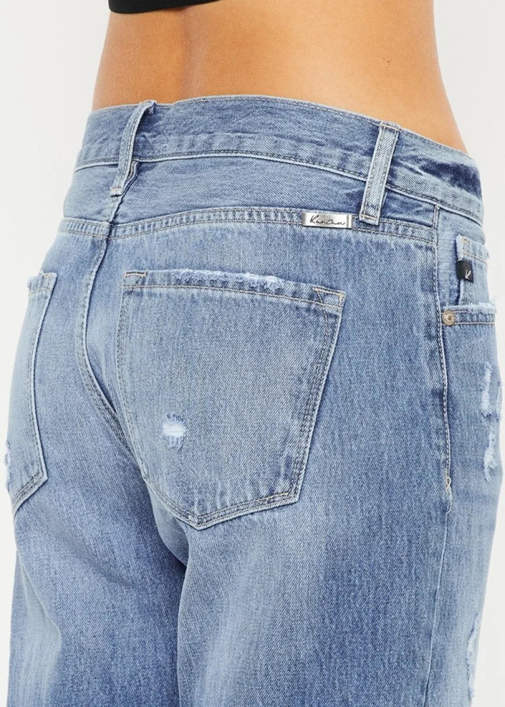 Close-up of light wash distressed denim jeans with frayed hem and visible pocket details.