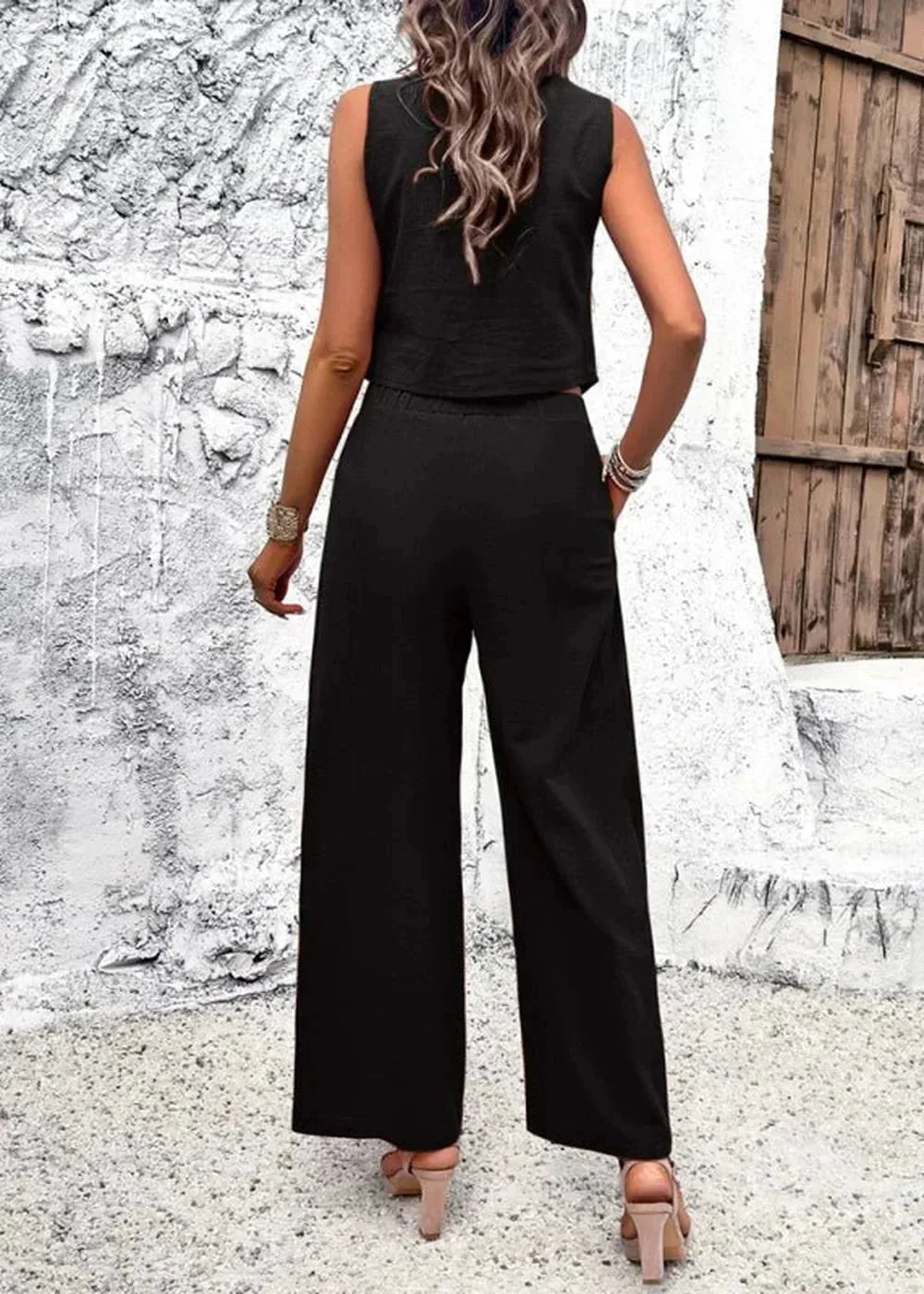 Back view of a woman wearing a black sleeveless crop top and black wide-leg pants.