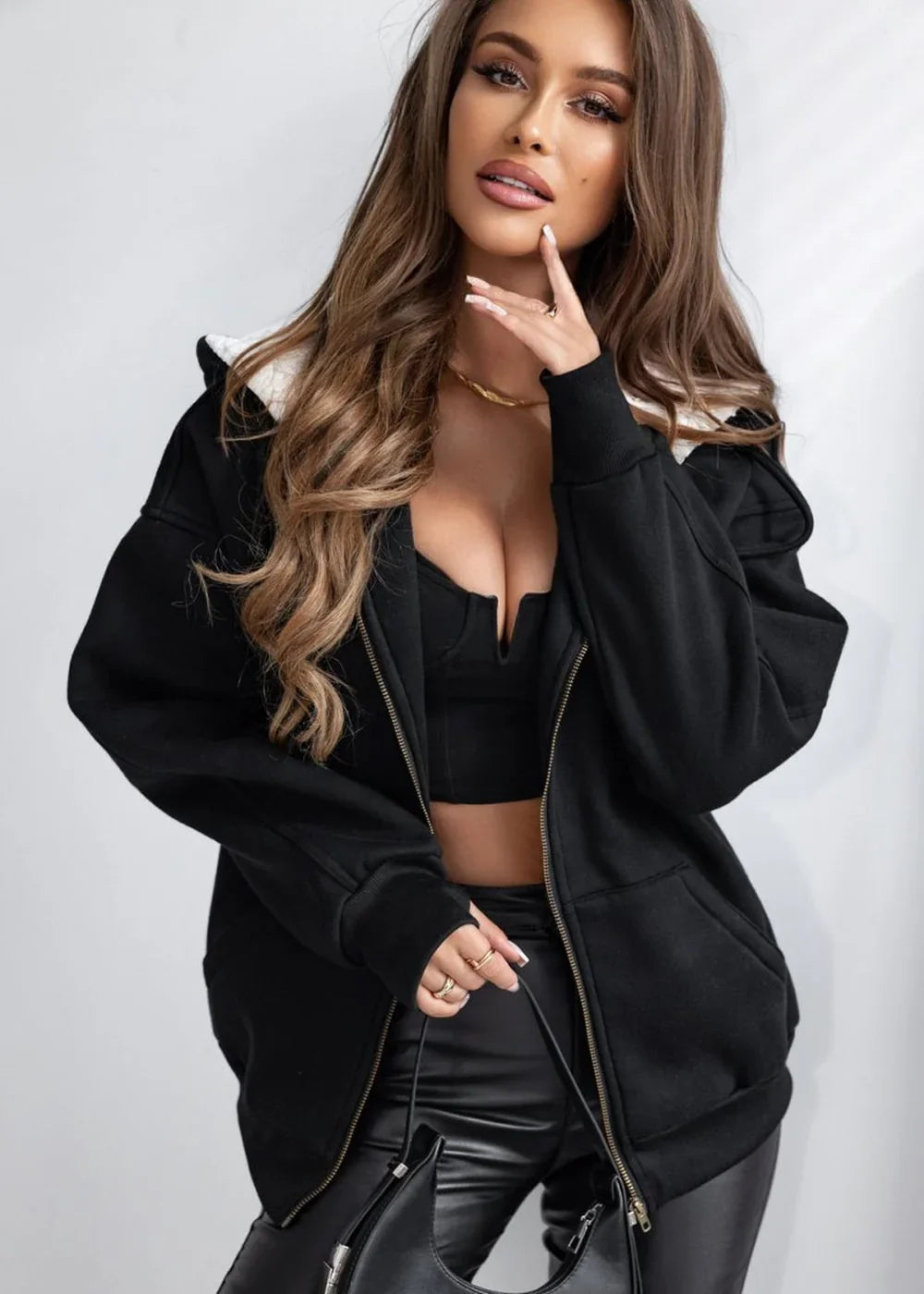 Black hooded zip-up jacket with sherpa lining, worn over a black crop top and faux leather pants.