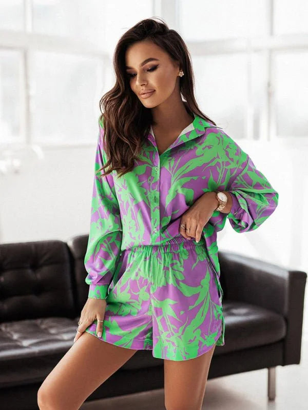 Woman in a vibrant purple and green floral print pajama set with a collared button-up shirt and elastic-waist shorts.