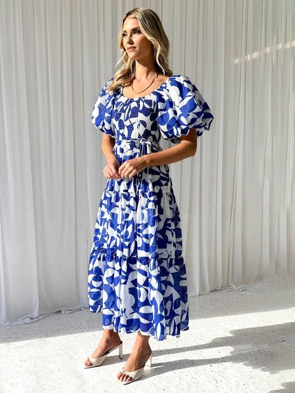 Woman in a blue and white abstract print maxi dress with puff sleeves and white block heel mules.