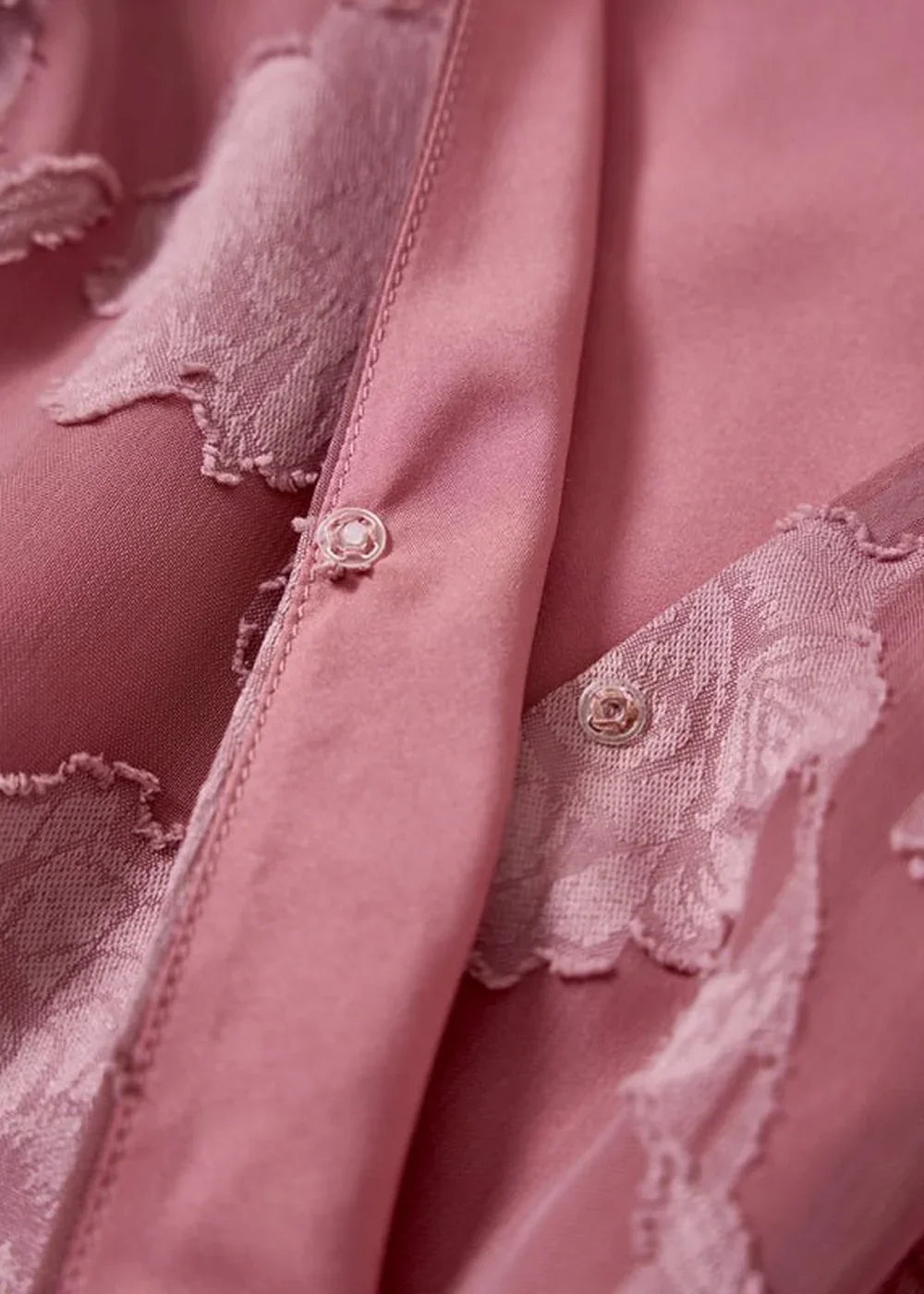 Close-up of a pink polyester dress with a floral print and ruffled trim, featuring pearl buttons.