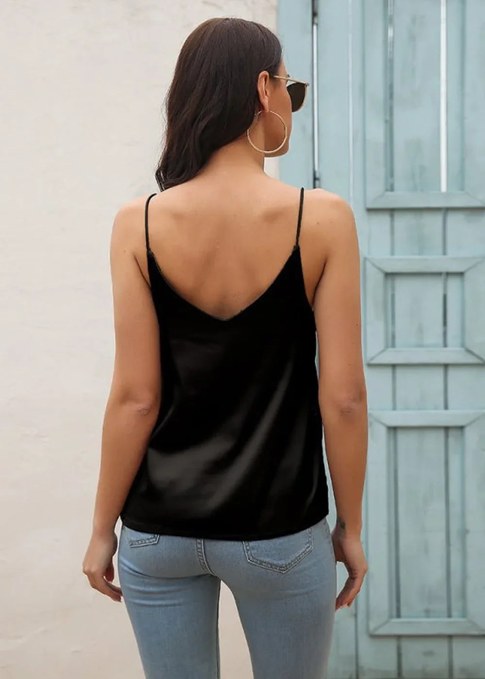Back view of a black satin camisole with spaghetti straps, paired with light wash denim jeans on a model.