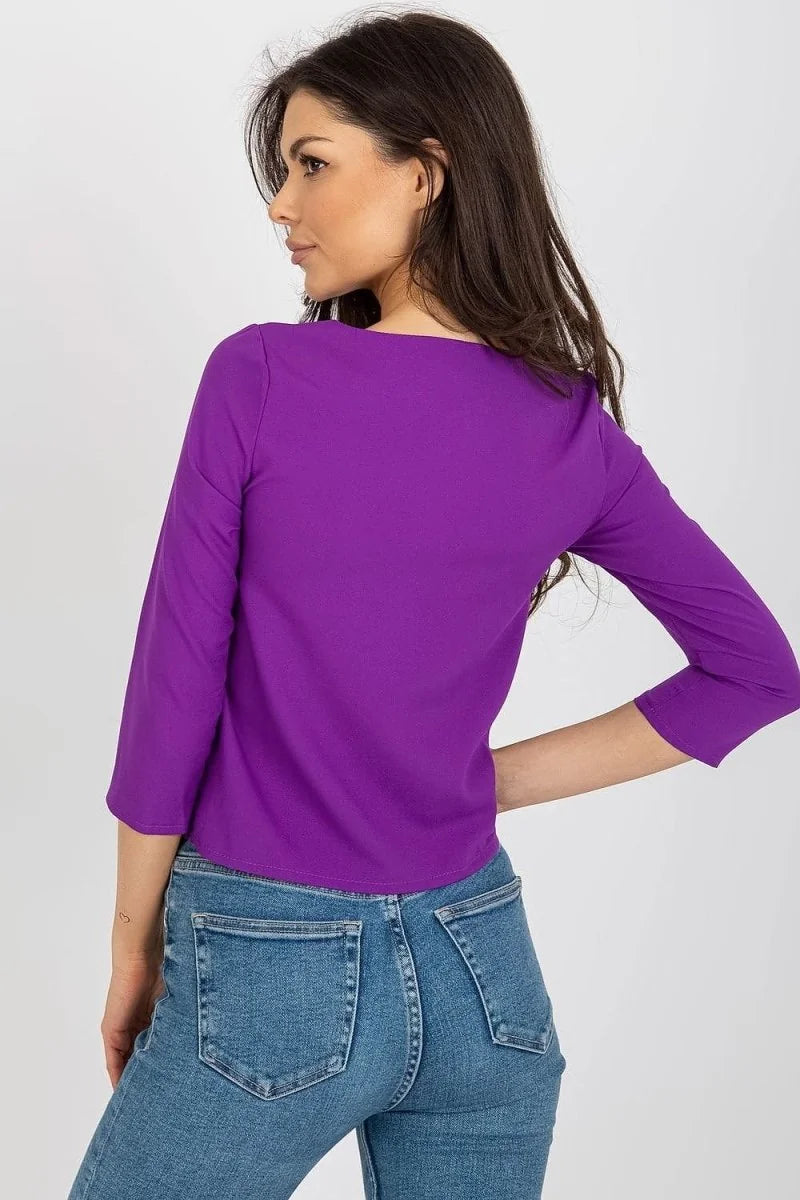 Back view of a woman wearing a vibrant purple three-quarter sleeve top and blue denim jeans.