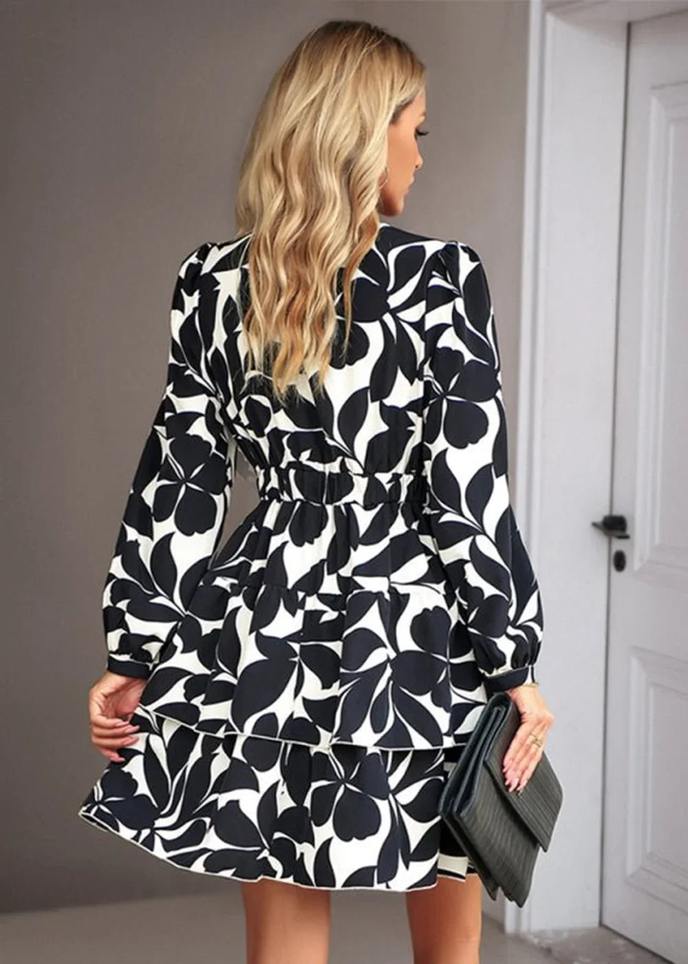 Black and white floral print mini dress with long sleeves and tiered skirt, worn by a model holding a black clutch.