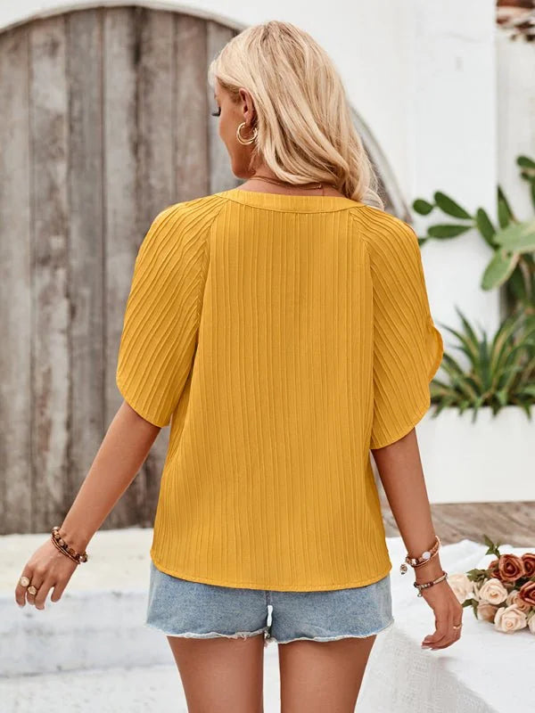 Back view of a woman wearing a bright yellow textured short-sleeve top and denim shorts.