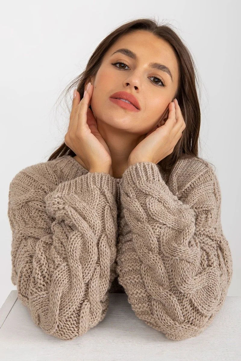 Close-up of a woman wearing a beige knit sweater with intricate cable knit sleeves and a textured finish.