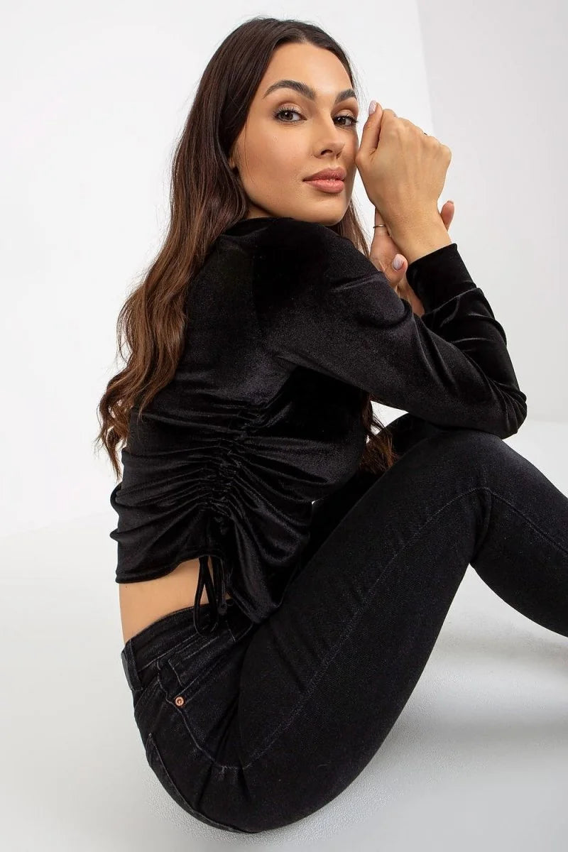 Black velvet ruched top with long sleeves, paired with dark wash denim jeans.