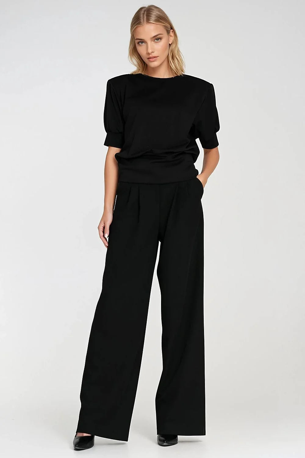 Full-length shot of a woman in a black oversized top with padded shoulders and wide-leg pants.