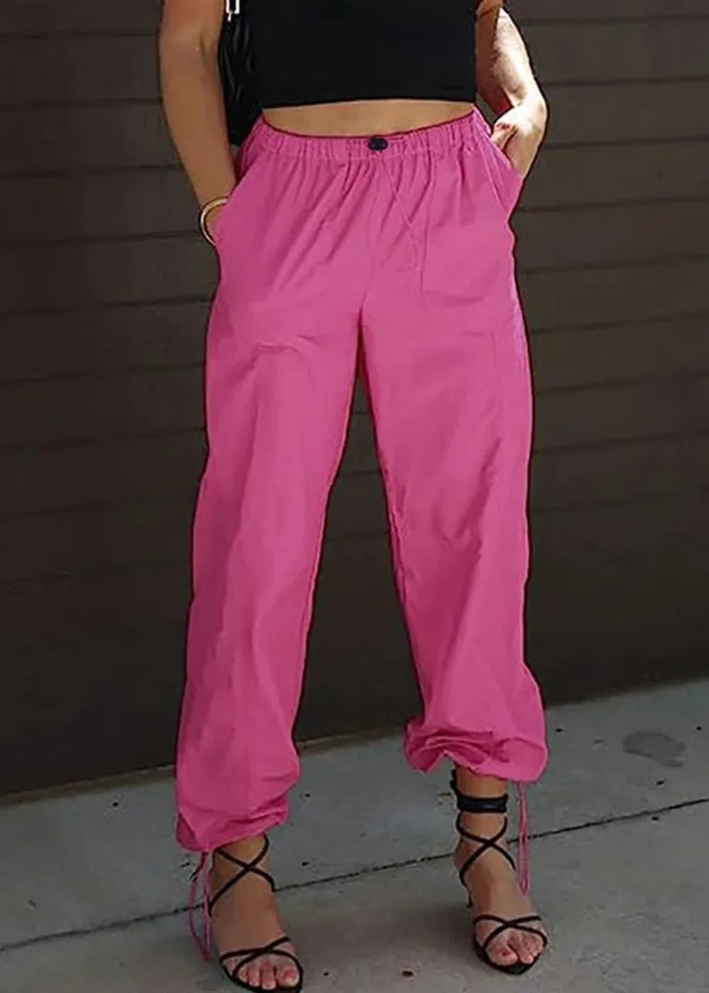 Bright pink cargo pants with drawstring ankles and black lace-up heels on model.