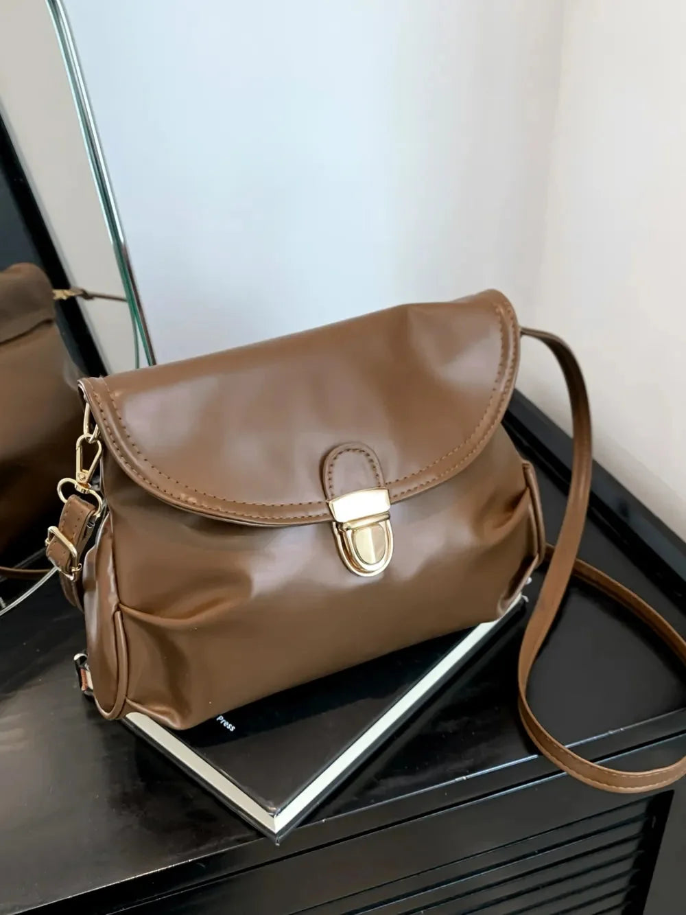 Shiny brown leather crossbody bag with gold clasp and adjustable strap.