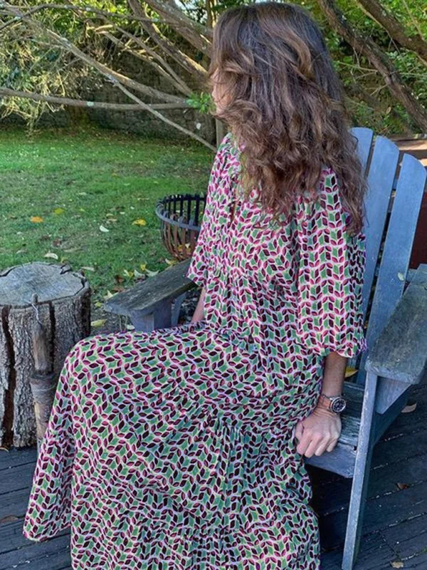 Woman in a flowy, knee-length dress with a geometric green, pink, and black pattern, sitting on a chair.