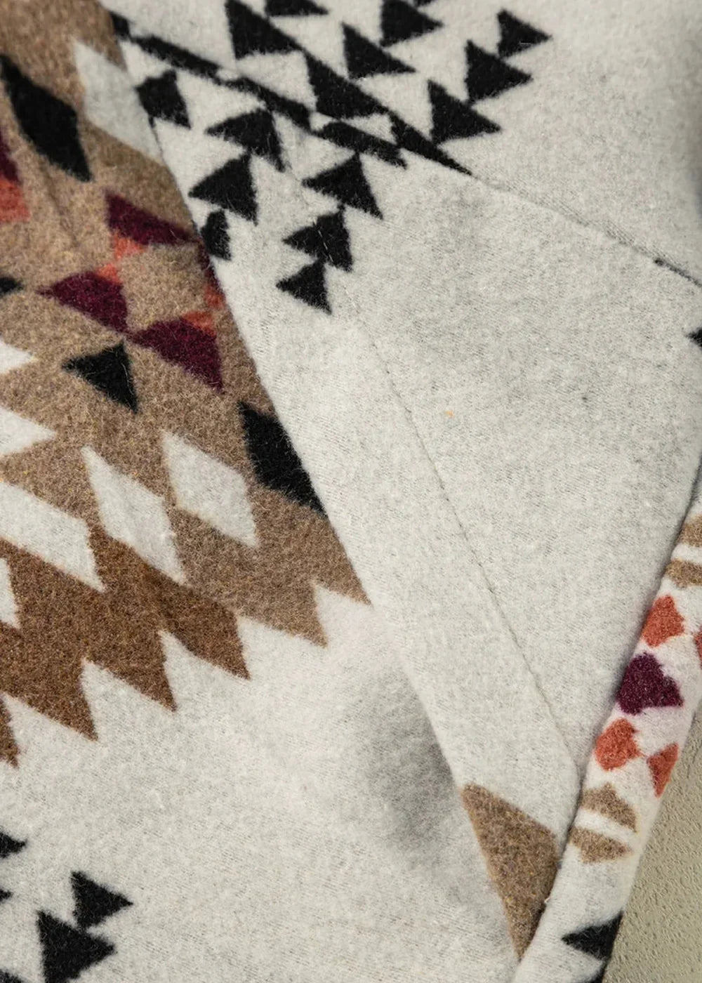 Close-up of a jacket with a geometric pattern in brown, black, and maroon on a light gray textured fabric.