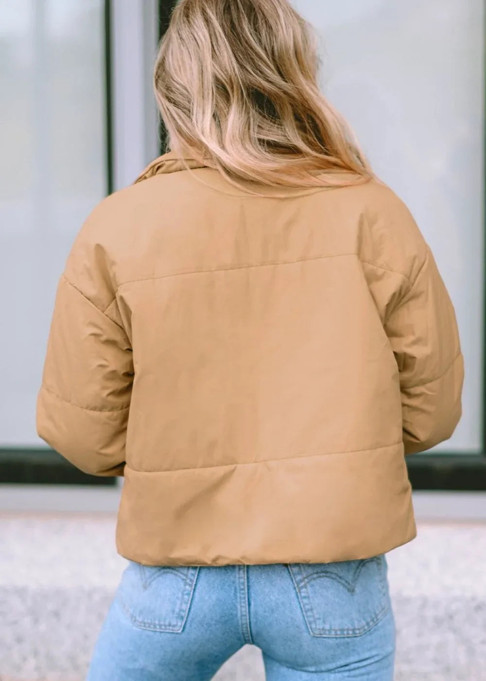 Back view of a tan puffer jacket on a model wearing light wash jeans.
