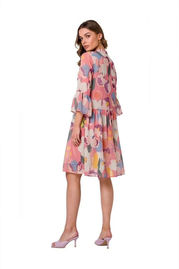 Pink dress with abstract floral print, bell sleeves, and tiered skirt, worn with light purple heels.