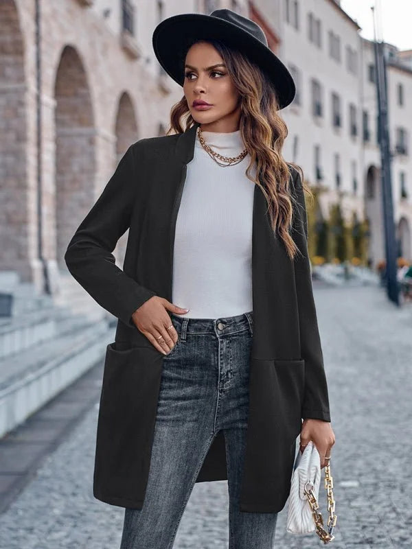 Black waterfall cardigan with textured fabric, pockets, and gold chain detail on handbag.