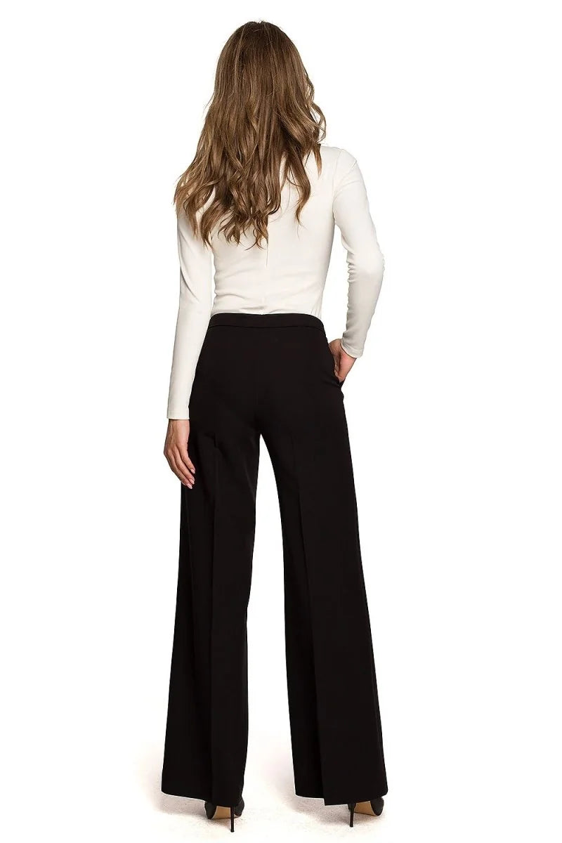 Woman from behind wearing black wide-leg pants and a white long-sleeve top.