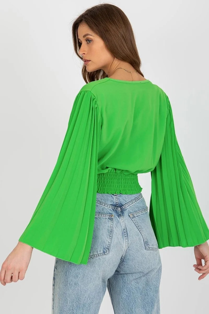 Lime green blouse with pleated bell sleeves and smocked waist, worn with light wash jeans.