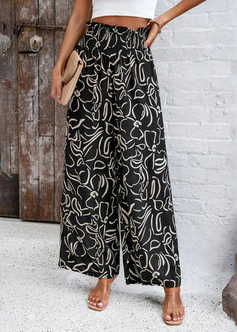 Black wide-leg pants with a white abstract floral print and smocked waistband.