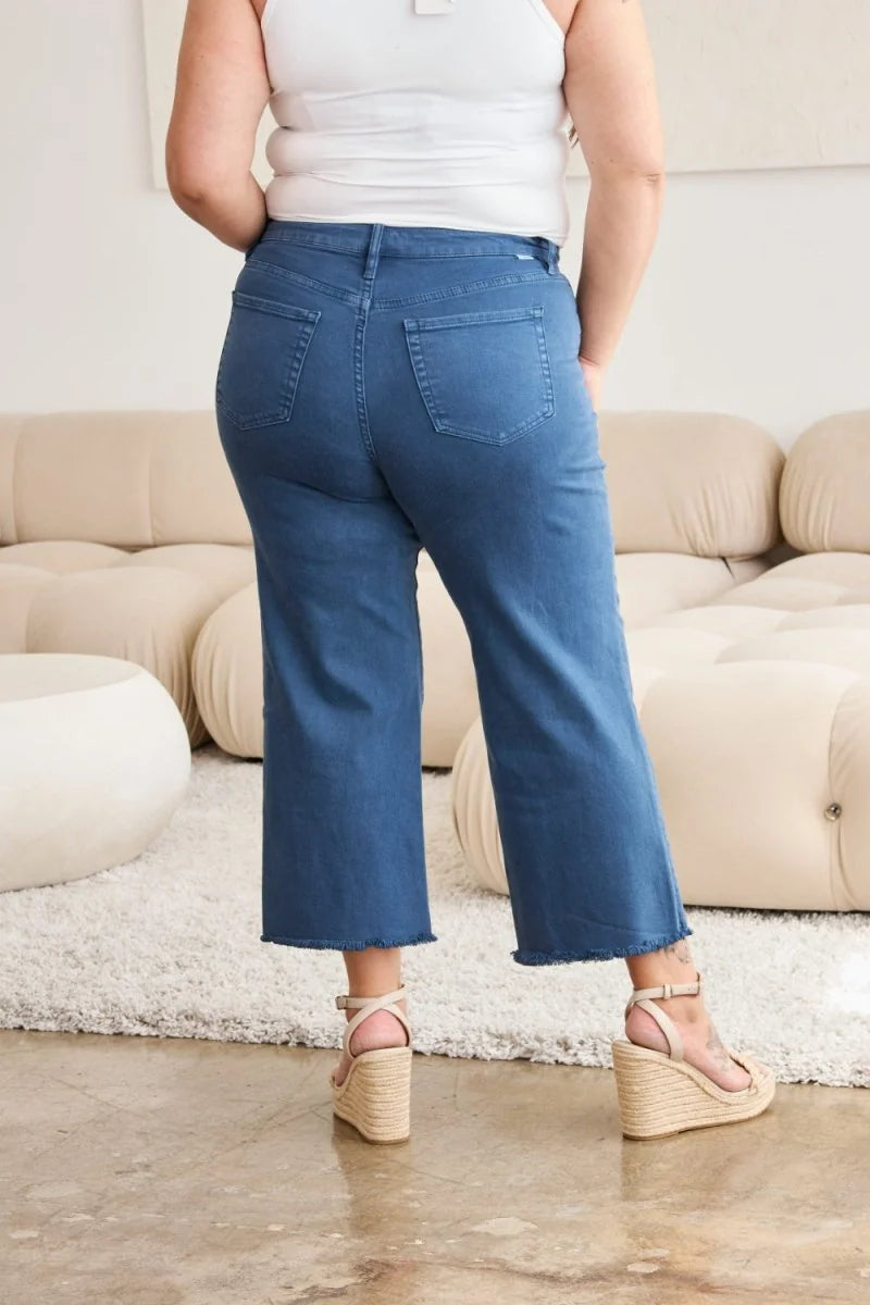 Back view of blue denim crop jeans with frayed hem, worn by a model with wedge sandals.