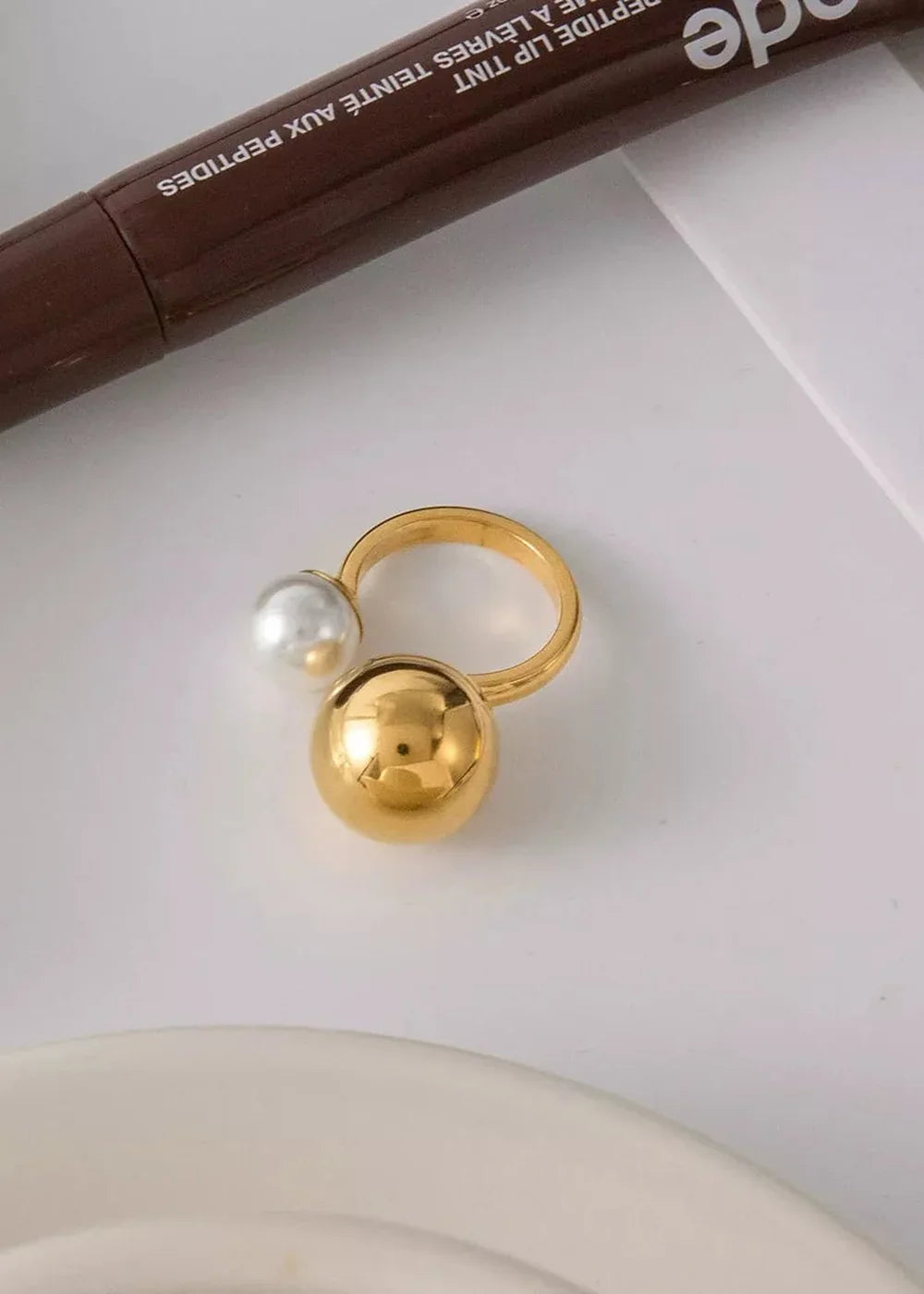 Gold ring with pearl and gold bead accents on a white surface.
