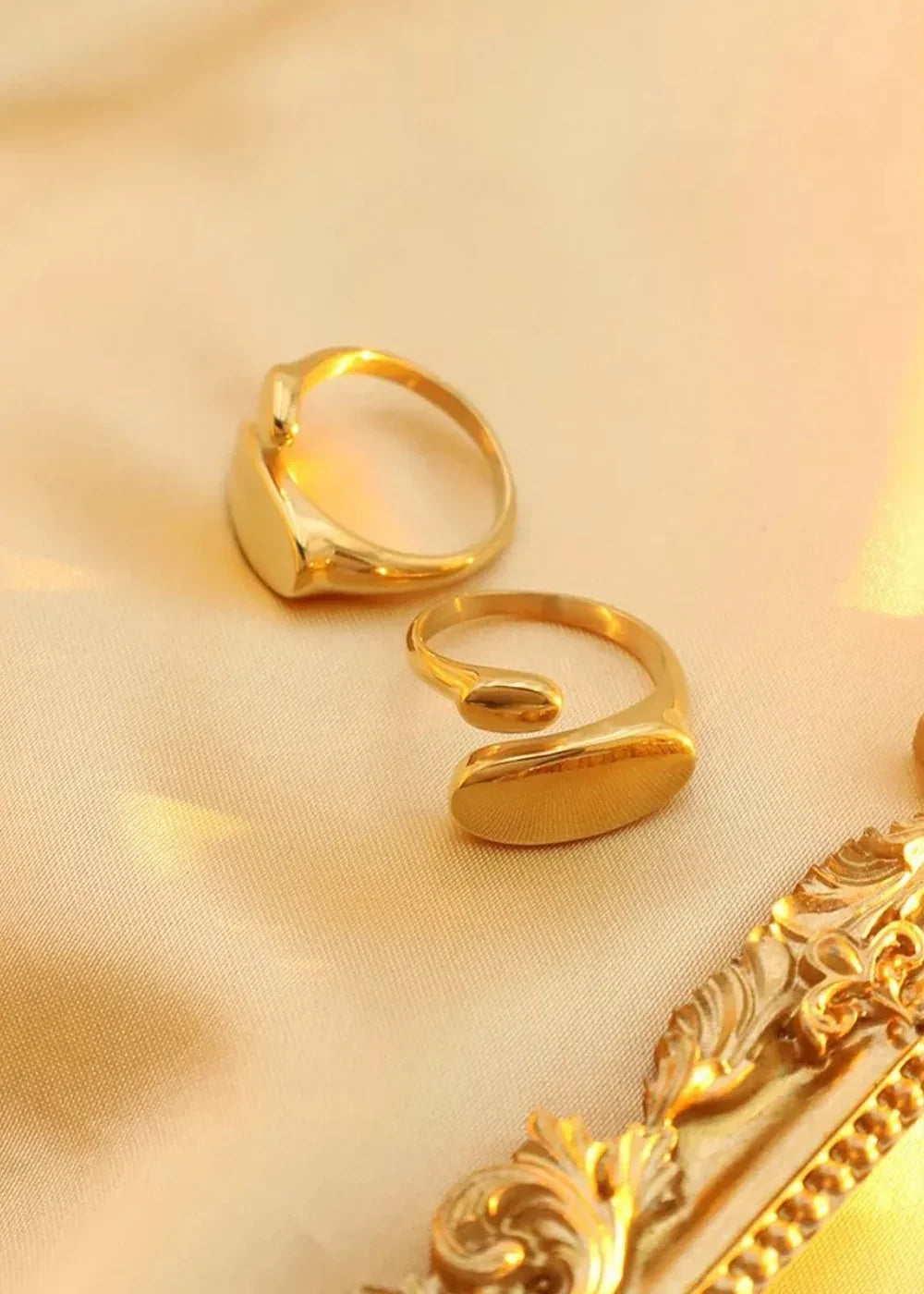 Two gold-plated titanium steel rings on a silky gold background with ornate gold trim.