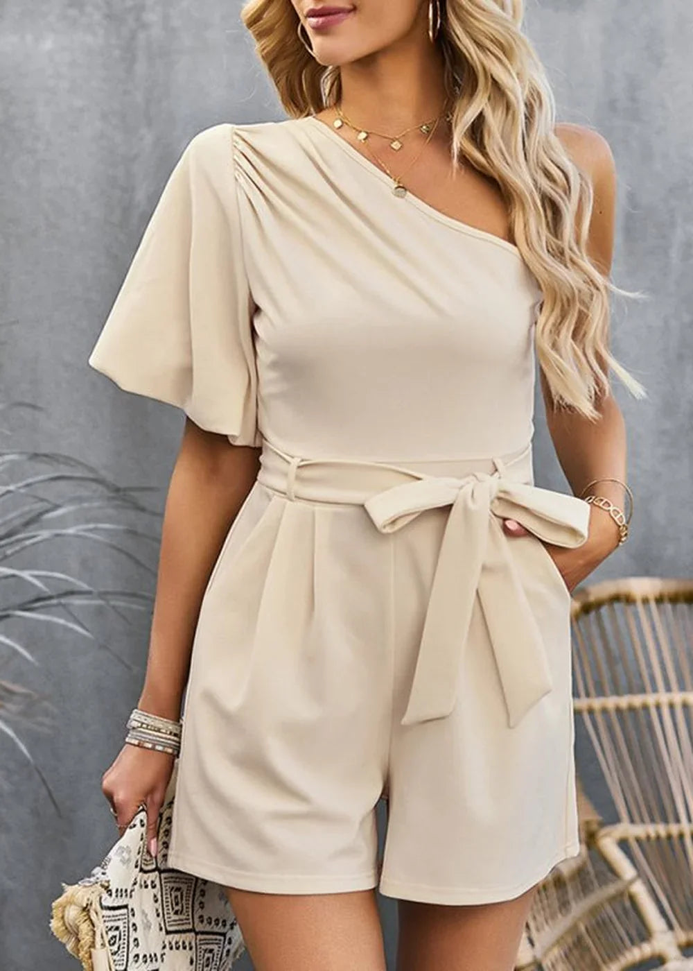 Cream one-shoulder romper with a tie waist and flutter sleeves.