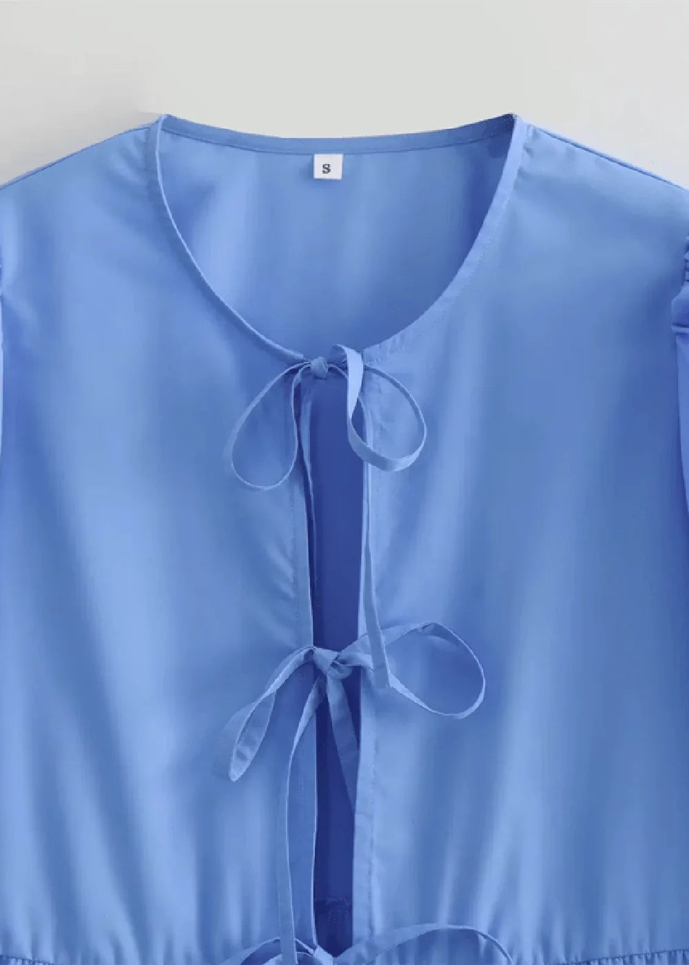 Close-up of a light blue polyester top with a V-neck and two tie closures at the neckline.