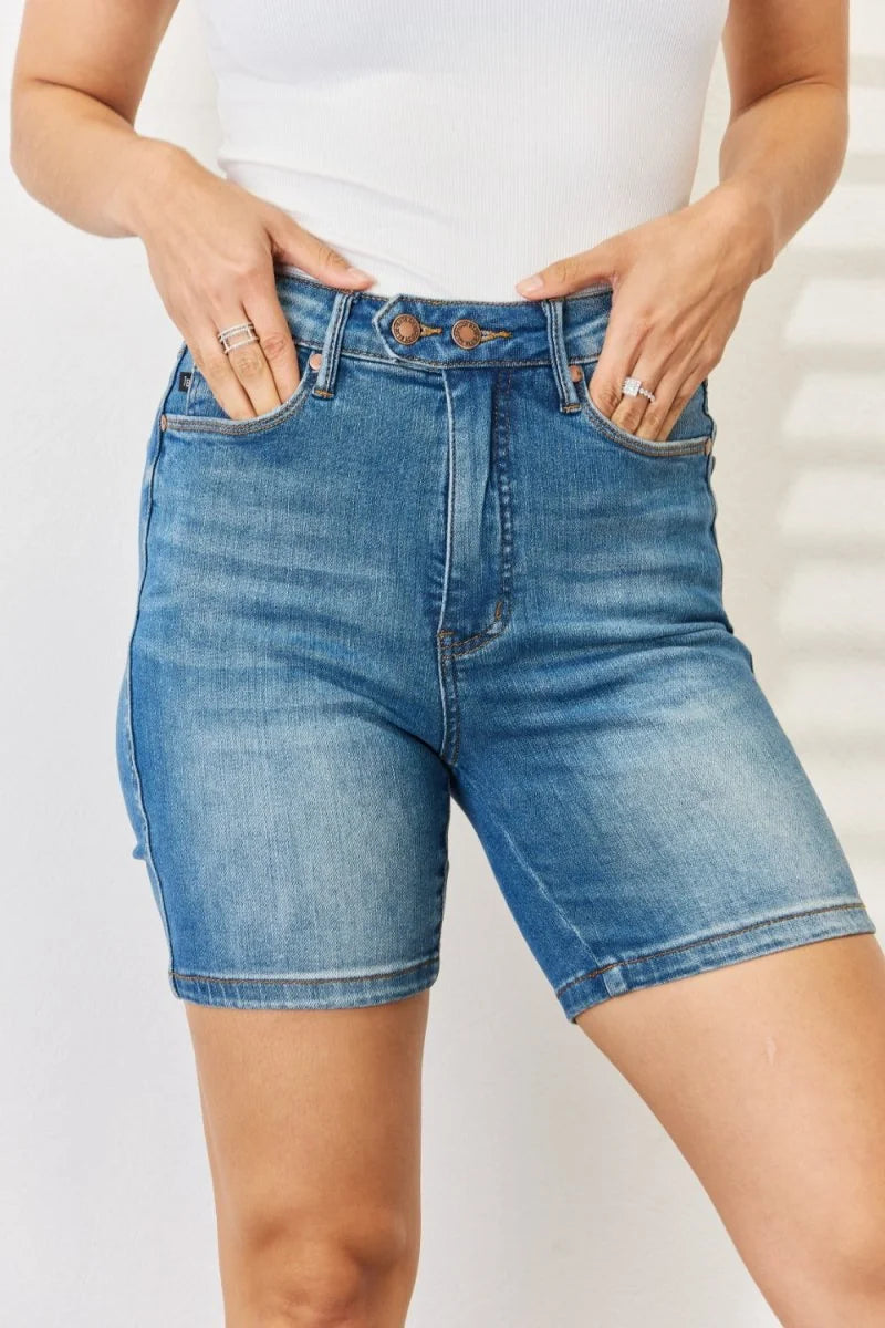 Close-up of medium-wash denim bermuda shorts with a high rise and button fly, on a model.