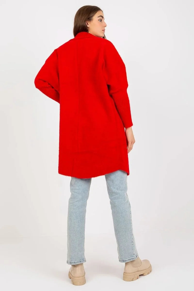 Back view of a bright red, textured, longline cardigan with ribbed cuffs, worn over light wash jeans.