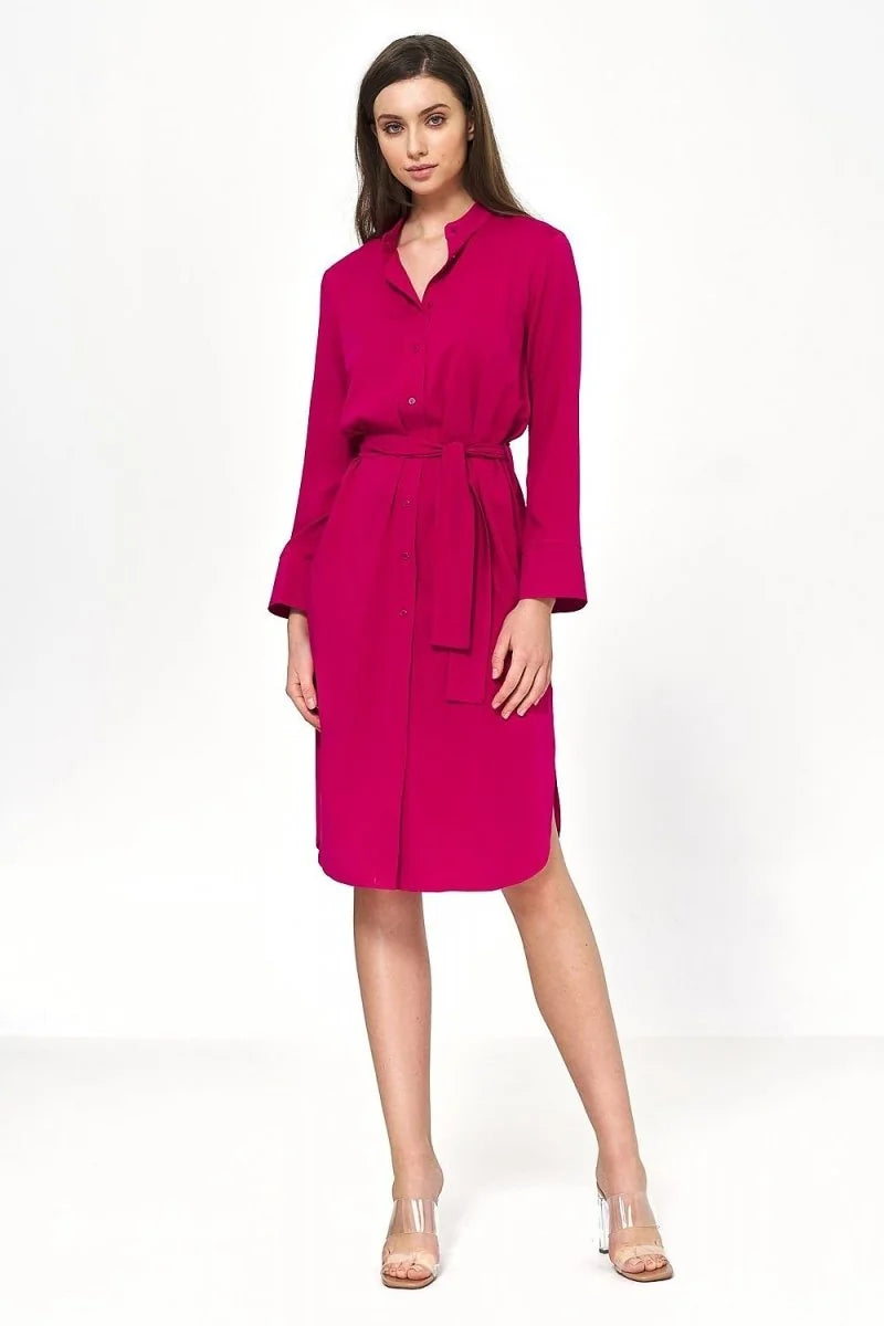 Full length shot of a woman wearing a bright pink viscose shirt dress with a belted waist and clear heels.